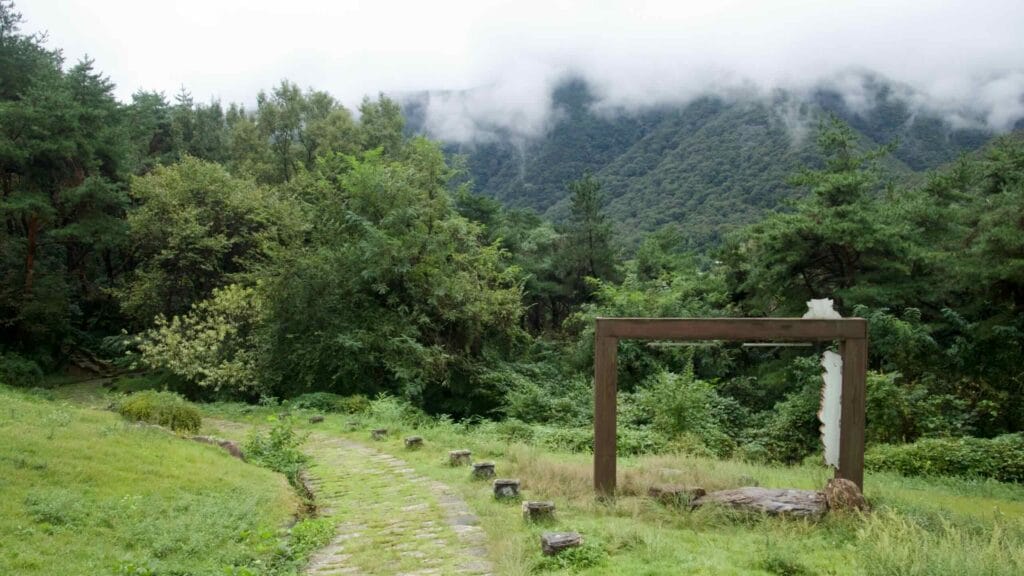 Low clouds cross the Sobaek Mountains beyond a grassy stone path and wood frame.