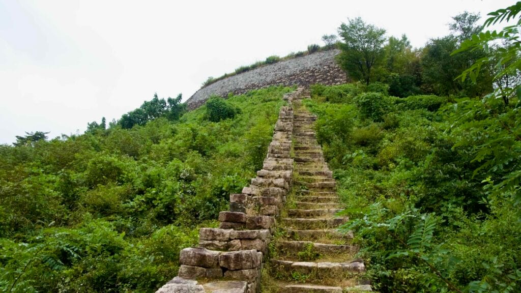 A long stone stair runs up the mountainside along the fortress wall to the upper bastion.