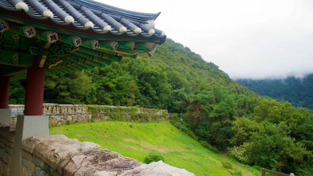 Pavilion eaves frame ramparts and a wooded valley at Gomo Fortress.