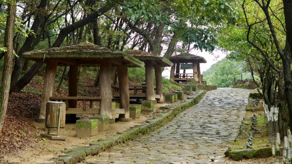 Thatched shelters line a stone path under trees at Mungyeong Saejae.