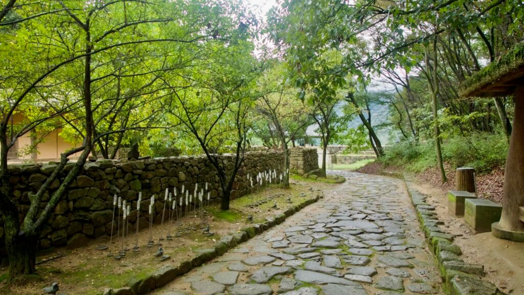 Stone paving leads between low walls and tree canopies near Gomo Mountain Fortress, where small placards and benches line the walk.