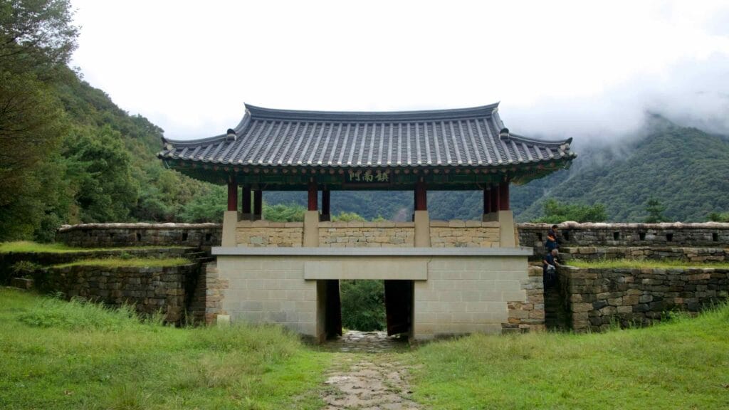 A gate pavilion stands above the stone south gate of Gomo Mountain Fortress in Mungyeong Saejae, framed by wooded slopes and mist.