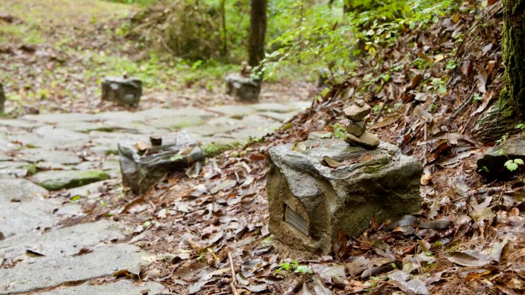 Small rock cairns rest on square pedestals beside the stone road in Mungyeong Saejae, with fallen leaves and wet earth softening it.