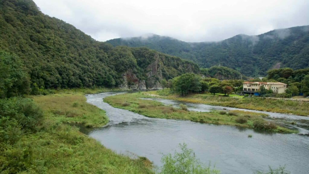 The Namhangang River bends beneath misty forested hills near Mungyeong, with a riverside villa and meadows along the bank.