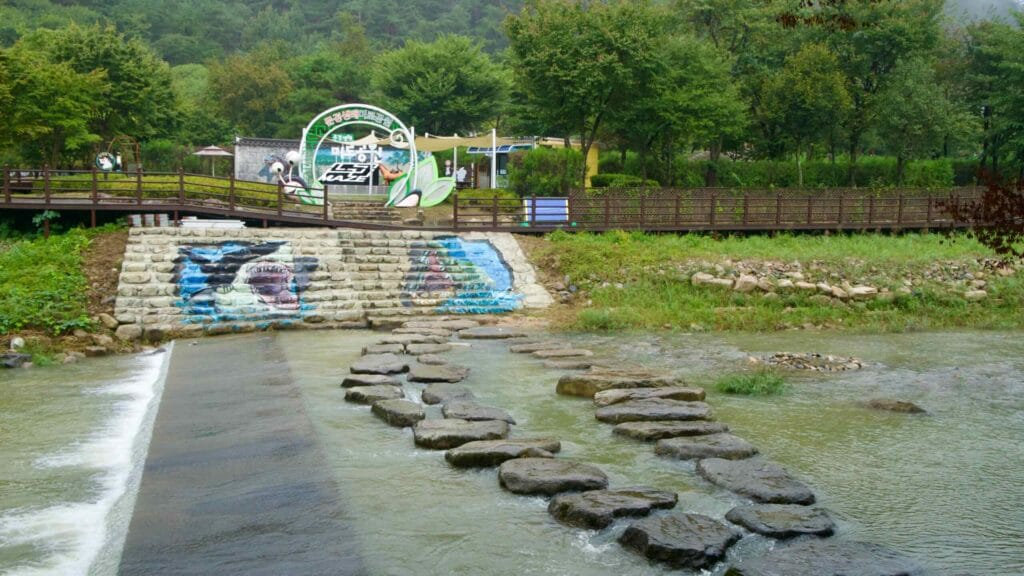 Stepping stones cross a stream beneath the Mungyeong Ecological Maze Park archway.