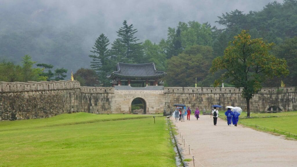 Visitors in ponchos approach Juheul Gate as fog rolls over the fortress walls.