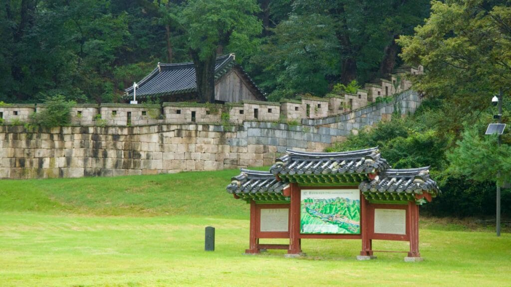 A traditional-roofed information board stands below stepped ramparts at Mungyeong Saejae.