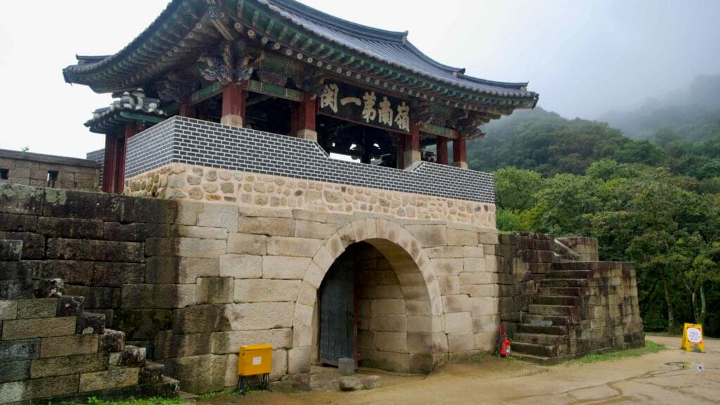 A gatehouse pavilion and stone steps emerge from fog at Mungyeong Saejae.