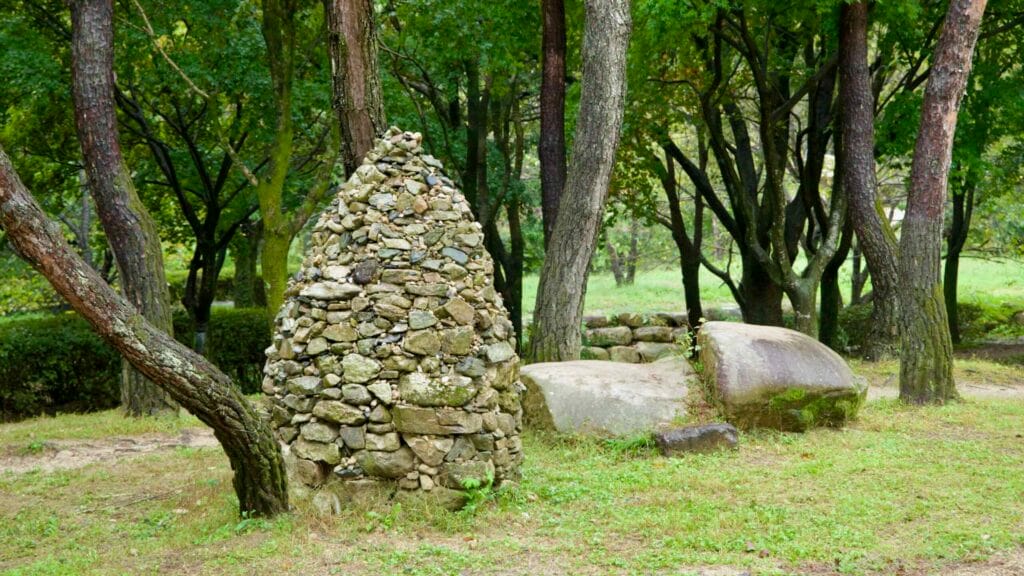 A conical stone cairn stands between pines at Mungyeong Saejae Provincial Park.