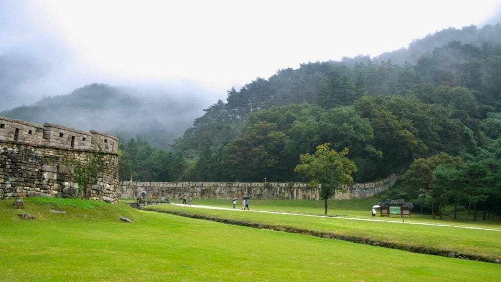 Mist rolls over forested hills behind the stone fortress wall at Mungyeong Saejae.