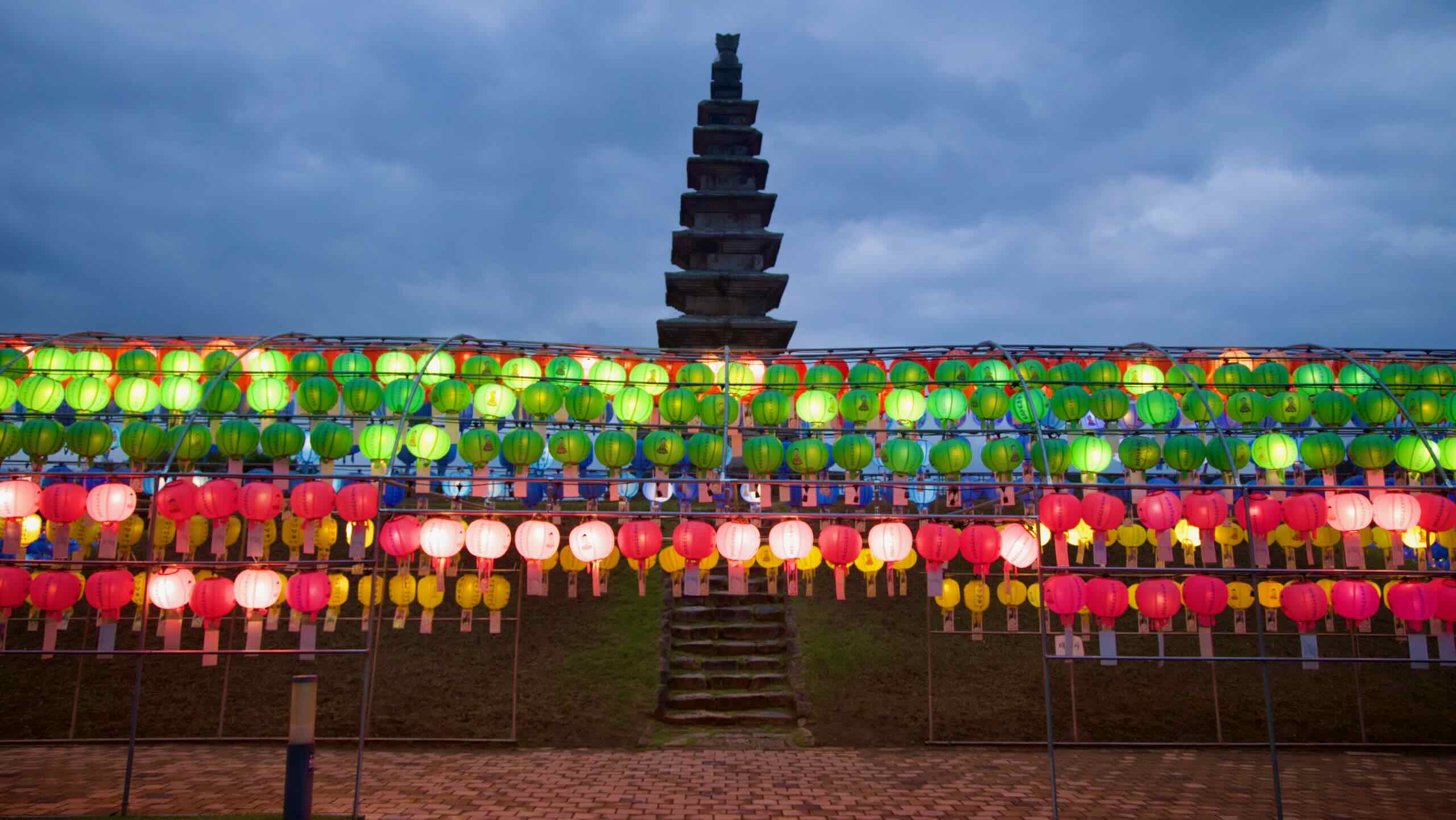 Lantern bands stretch before Jungang Tower with a central stairway rising from the brick path.
