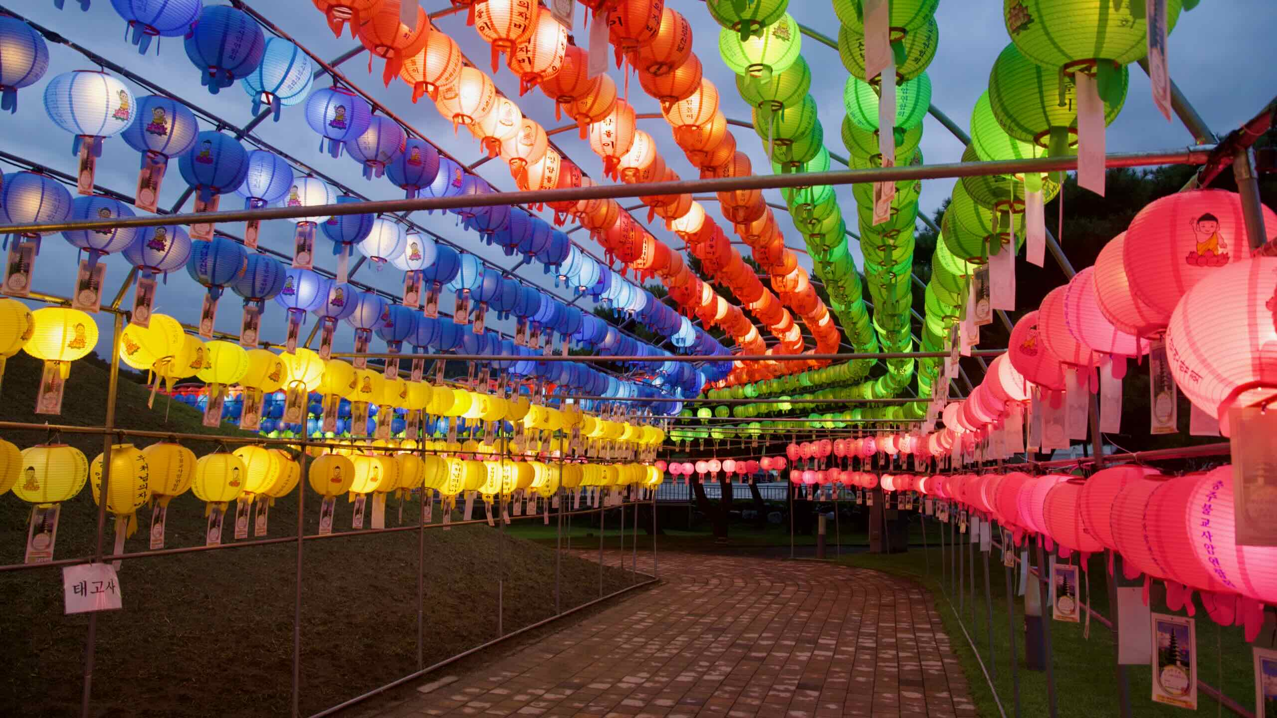 Rows of multicolored lanterns form a canopy above a curving brick walkway at Jungangtap Park.