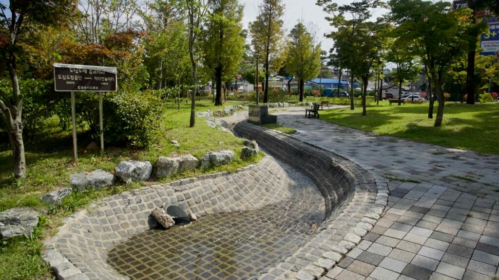 A stone-lined water channel winds through a small urban park in downtown Chuncheon.