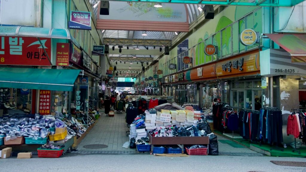 A view down the covered aisles of Chuncheon Jungang Market shows stacks of shoes and clothing stalls.