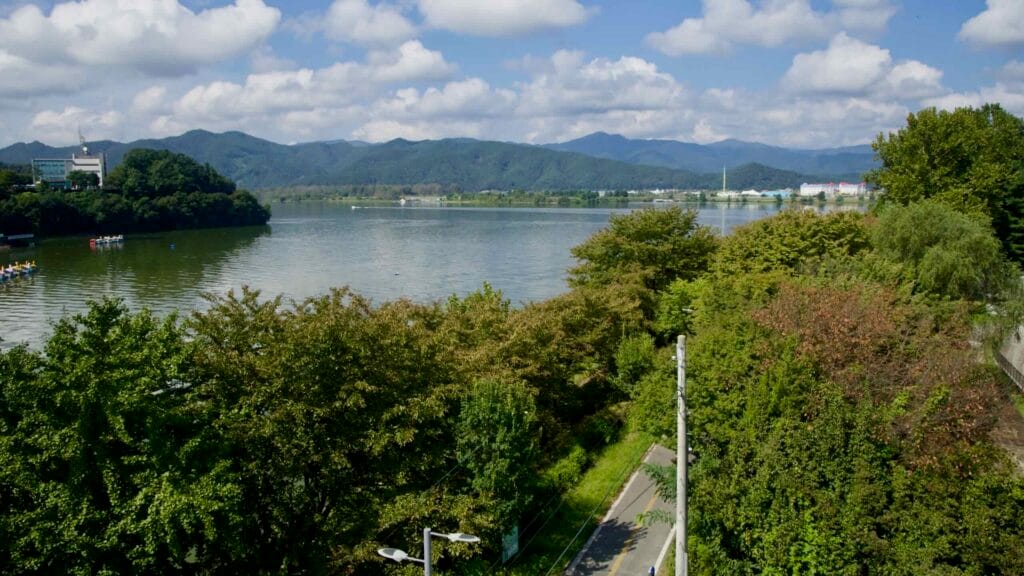 A broader view from Sairo 248 bridge looks over Lake Uiam, shoreline trees, and distant ridges.