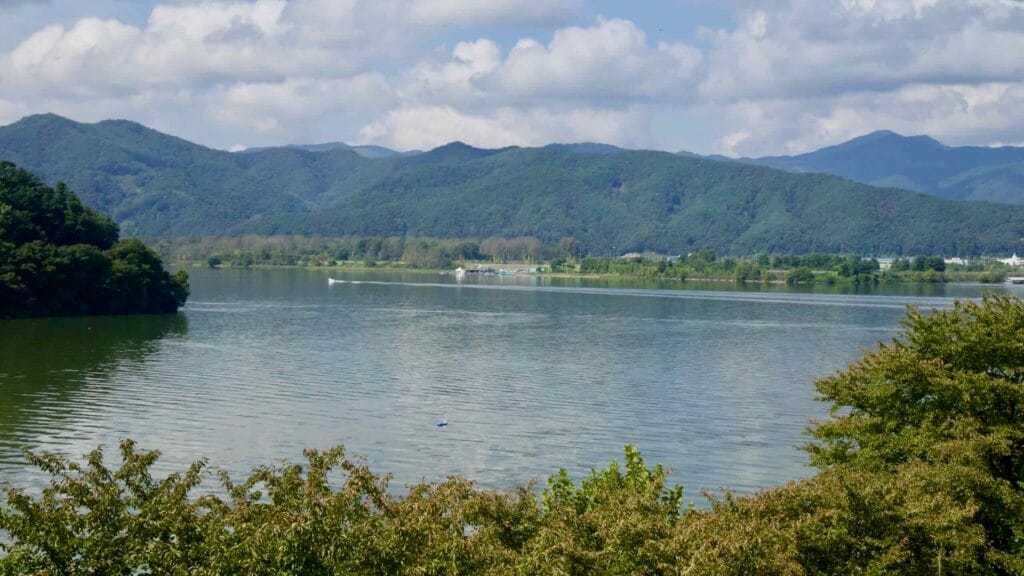Lake Uiam fills the frame beneath layered green ridges and scattered clouds near Chuncheon’s Sairo 248 bridge.