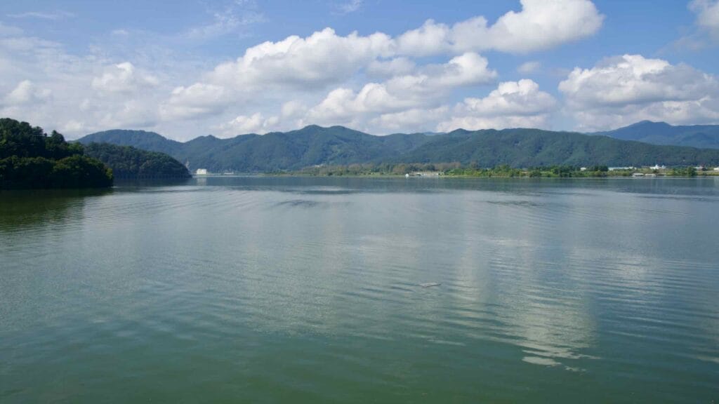 Lake Uiam stretches west beneath a blue sky, its rippled surface reflecting clouds and surrounding green hills.