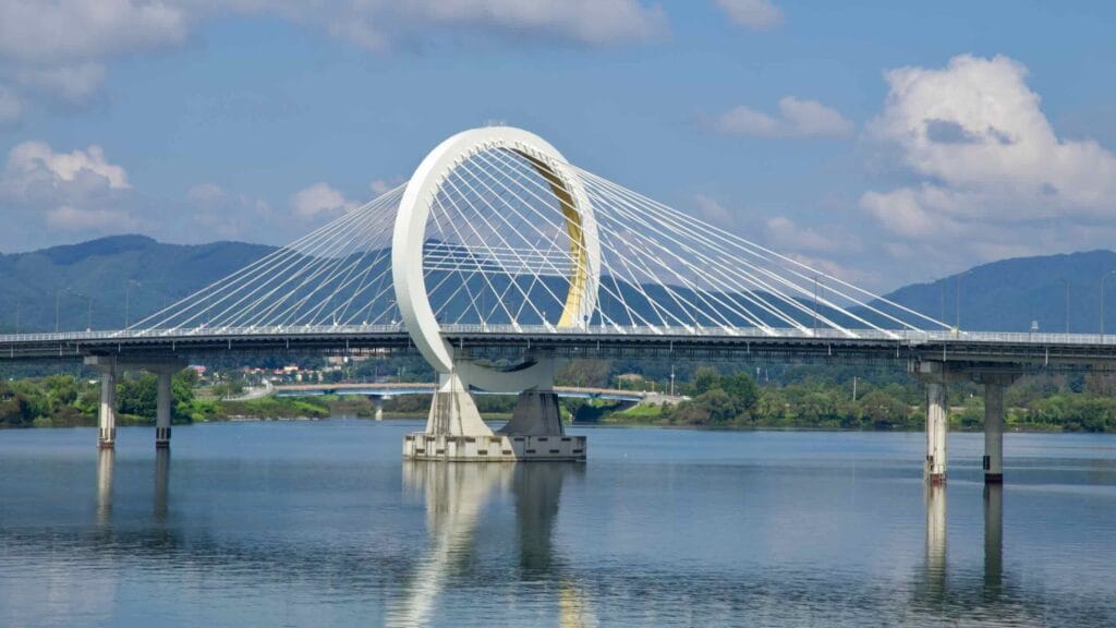 A paved promenade curves through Chuncheon’s lakeside park with views toward low surrounding hills.