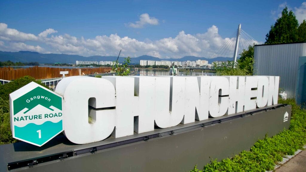 A large CHUNCHEON sign marks the riverfront near Soyang River Skywalk beside Uiam Lake and apartments.