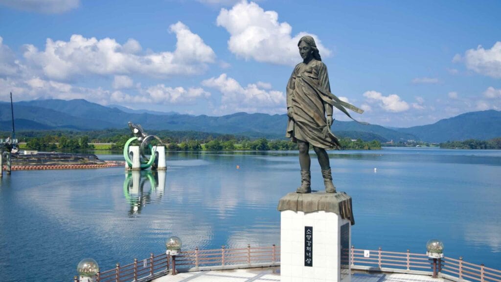 The Soyang River Maiden statue stands above Uiam Lake with forested hills beyond.