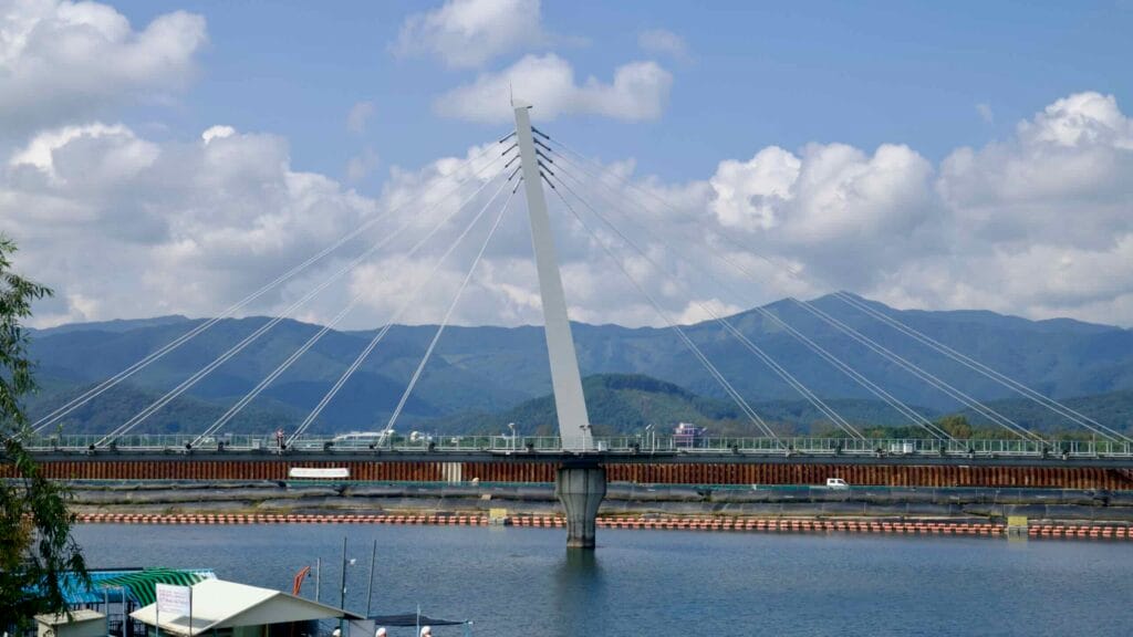 The cable-stayed pylon of Chuncheon’s bridge rises from Lake Uiam with fan-shaped cables and mountain horizons.