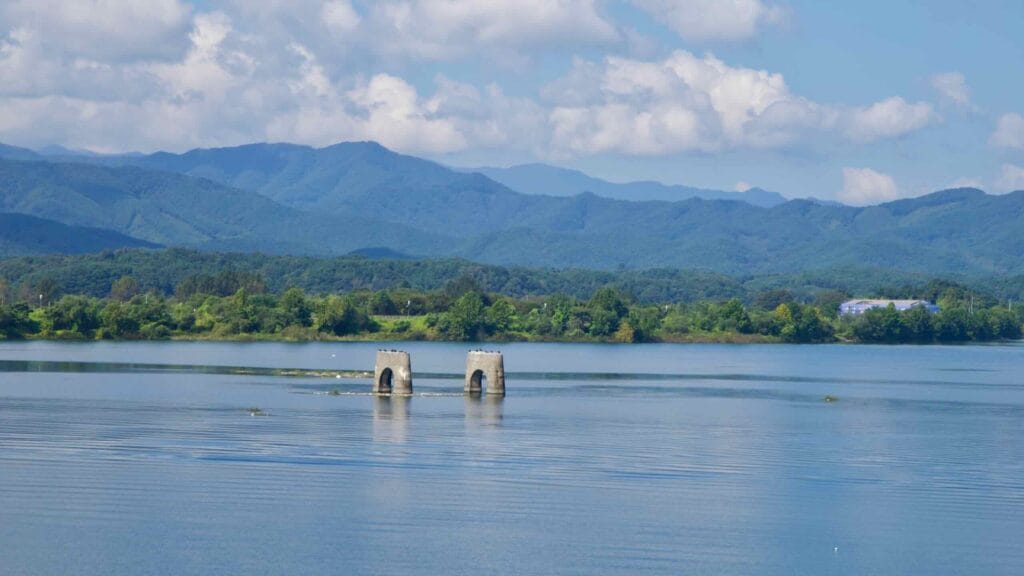 Two small stone piers or old sluice remains rise from Lake Uiam near Chuncheon, framed by tree-lined banks.
