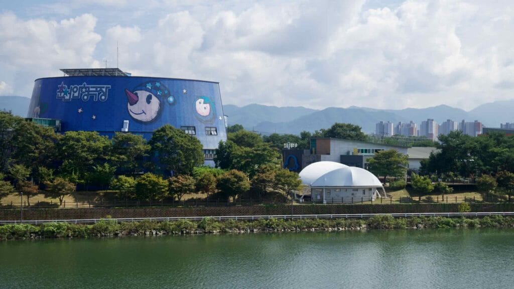 Chuncheon Puppet Theater is viewed across Uiam Lake with hills and apartments beyond.