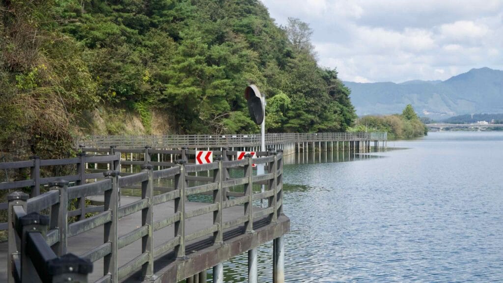 Mirror and chevrons at a bend as the boardwalk extends toward a distant bridge.