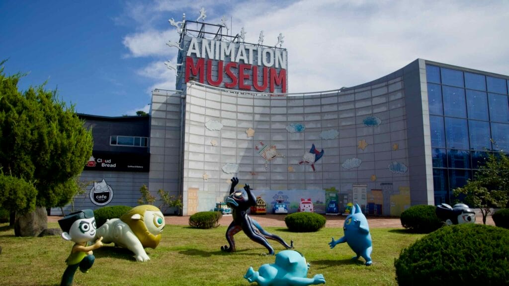 Character sculptures on the museum lawn with the curving facade behind.