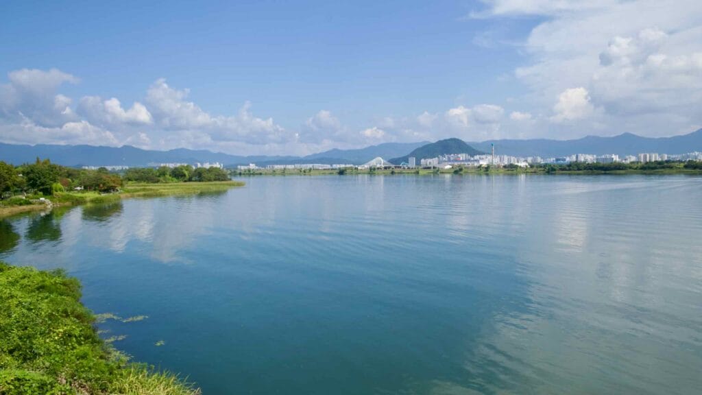 A view across the North Han River shows downtown Chuncheon with a bridge, Hajungdo, and apartment blocks.
