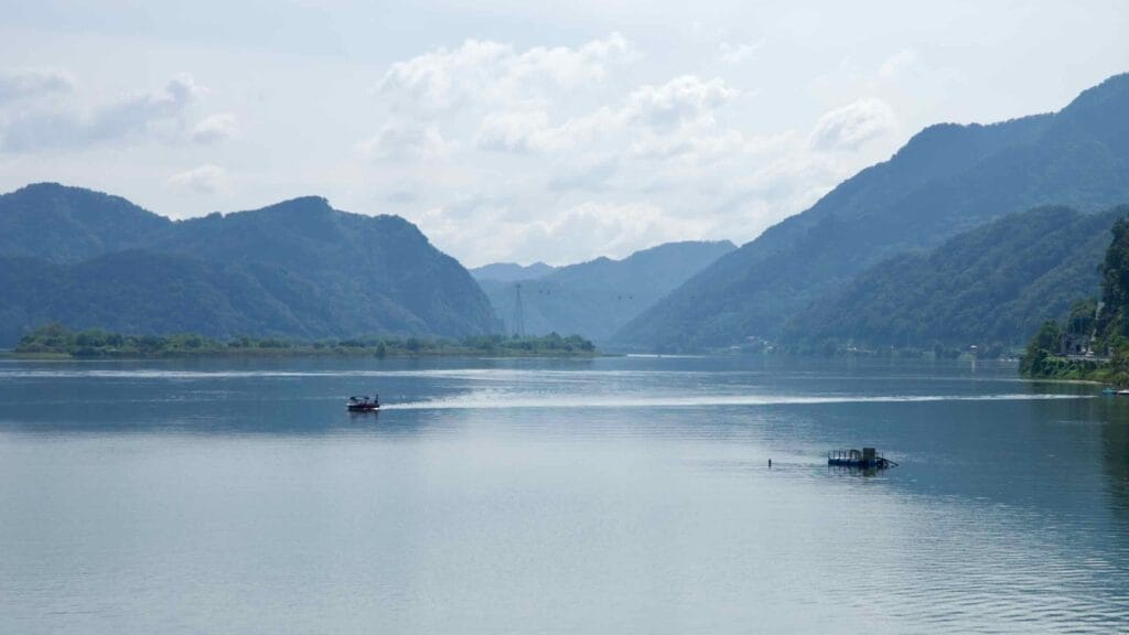 Small boats cross a calm reach of the Bukhangang between wooded ridges and low islands.