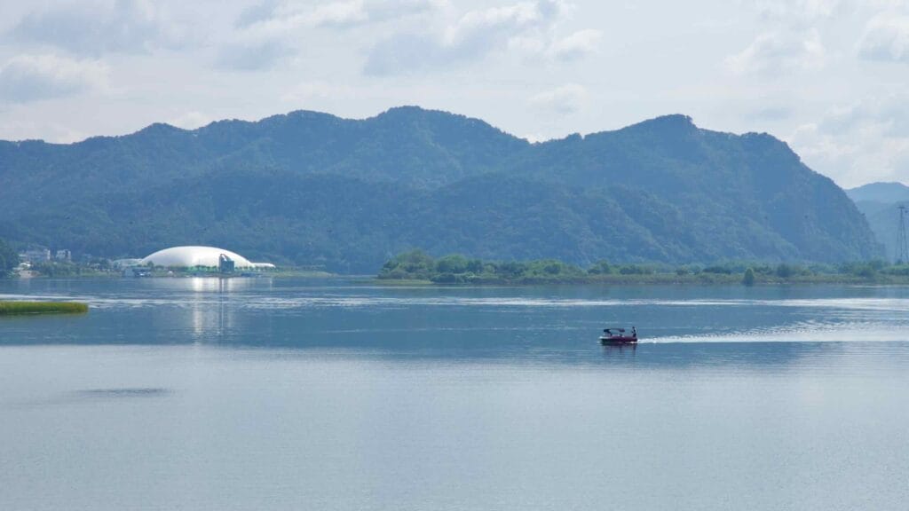 A small boat crosses Uiam Lake with a white domed structure on the far shore.