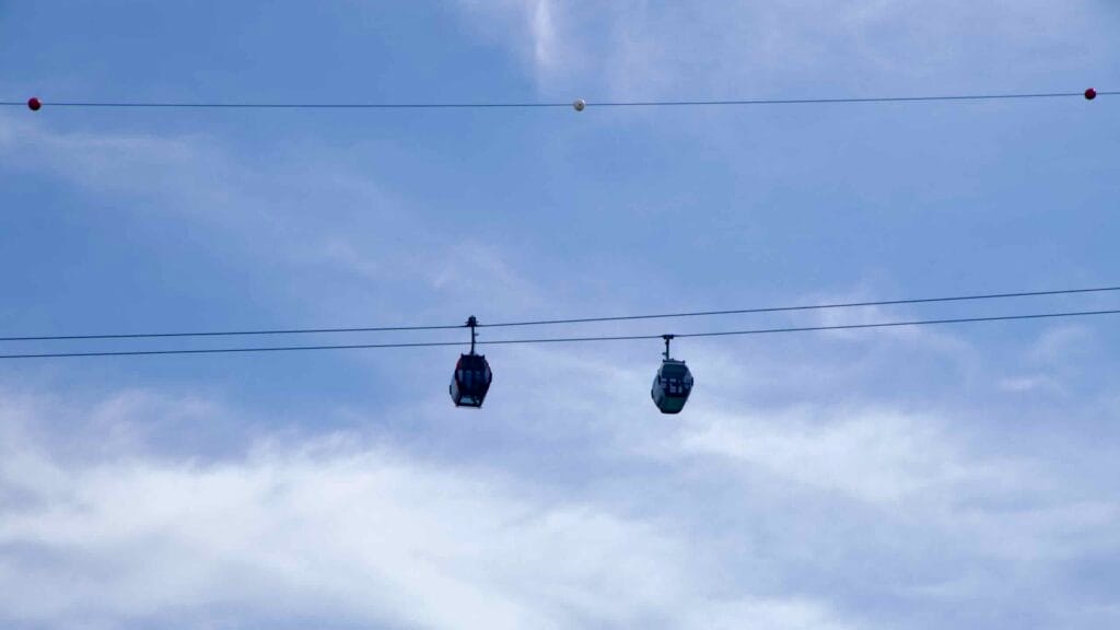 Two gondola cabins ride the Samaksan cable car against a pale blue sky.