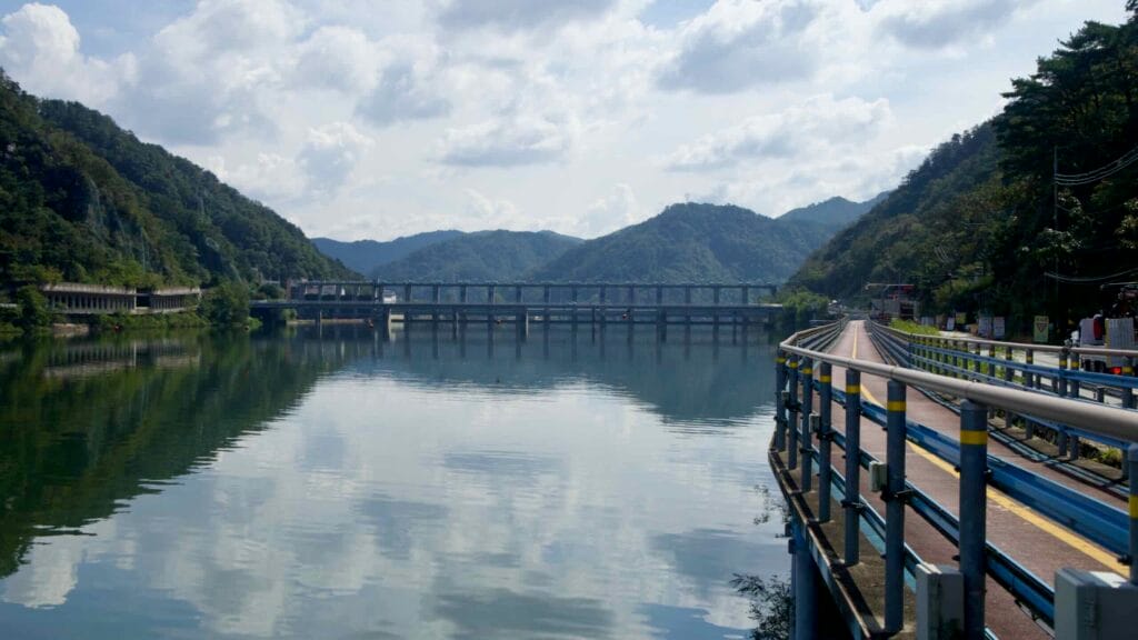 A broad panorama looks across Uiam Lake to Samaksan’s wooded flanks and a string of concrete gallery tunnels along the.