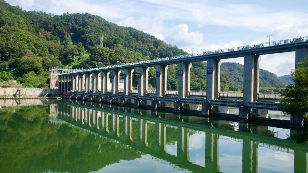 Pillars of Uiam Dam reflect on Lake Uiam under a bright sky.