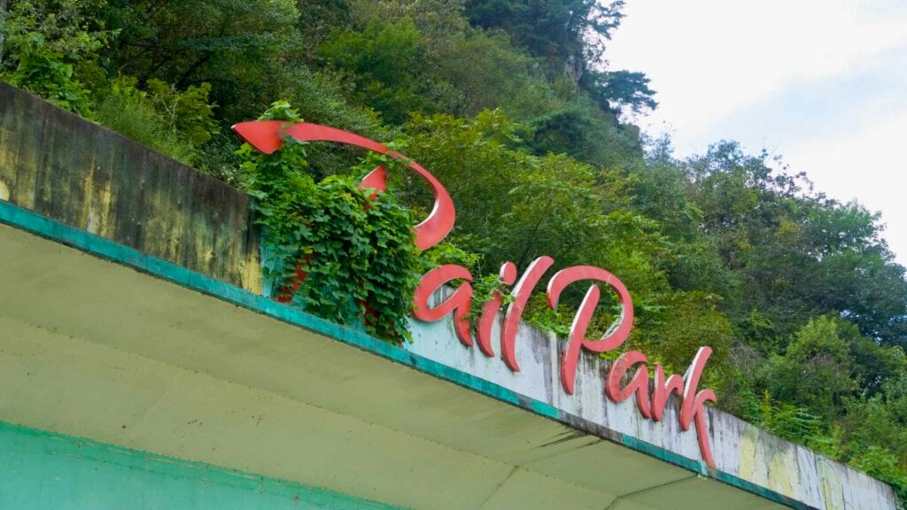 An old Rail Park sign peeks through vines near the former Gangchon Station by the river.
