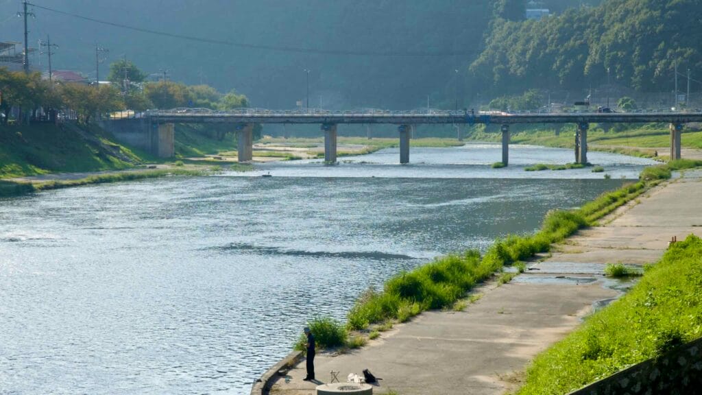 An angler stands on a riverside apron along Jojong Stream at Cheongpyeong, casting near the confluence with the Bukhan River.