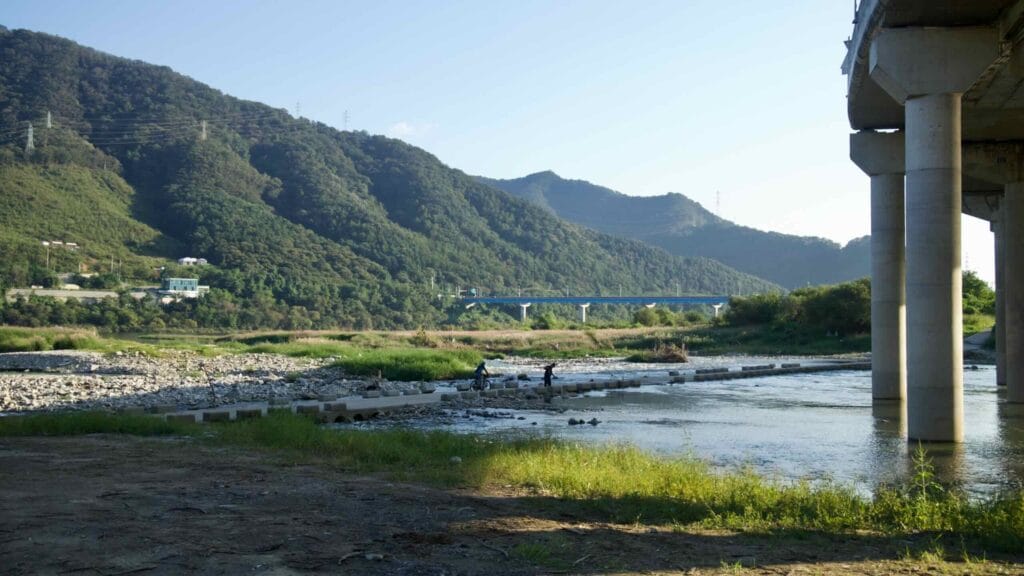 Cyclists and walkers pause on stepping blocks beneath Cheongpyeong 1 Bridge where Jojong Stream meets the Bukhan River.