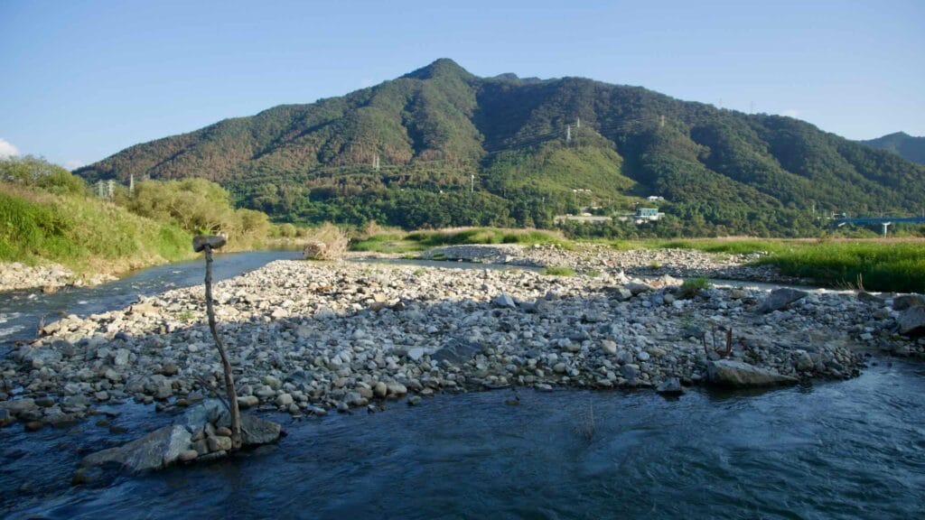 A shallow riffle curls around a stony gravel bar near the mouth of Jojong Stream, with a makeshift marker on a stick set in the stones.