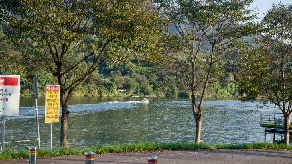 Signs and bollards mark a North Han River access point as a speedboat passes in the distance.