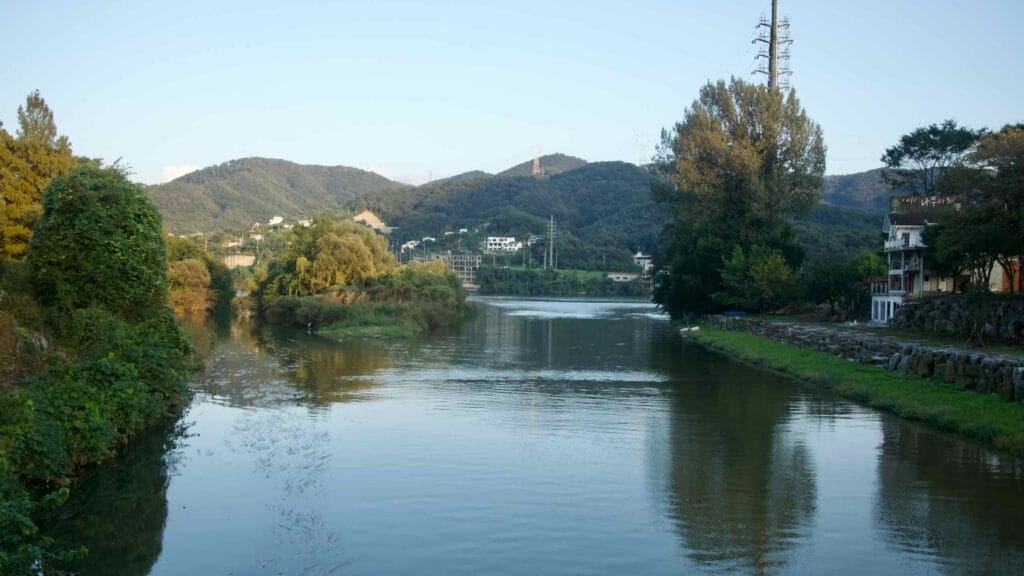 Evening light reflects on the Bukhan River in Namyangju with wooded hills and riverside homes.