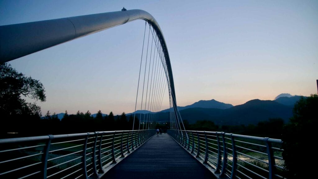 An arch pedestrian bridge crosses the Bukhangang at dusk.