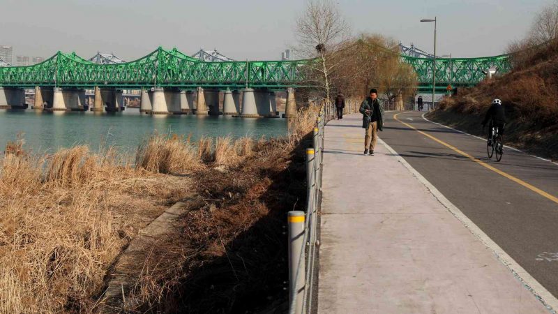 Walking and bike path along the Han River in Seoul. The Hangang Railroad Bridge spans the river in the background.
